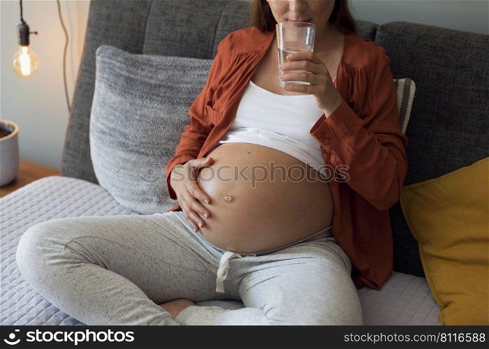 Pregnant woman holding glass of water relaxing in bed at home