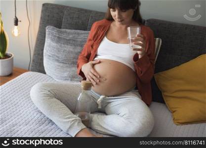 Pregnant woman holding glass of water relaxing in bed at home