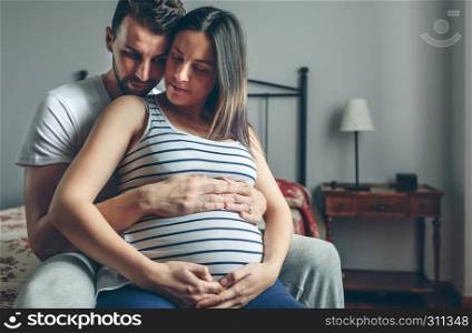 Pregnant woman holding her belly embraced by her husband. Pregnant woman embraced by her husband
