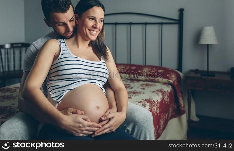 Pregnant woman holding her belly embraced by her husband. Pregnant woman embraced by her husband