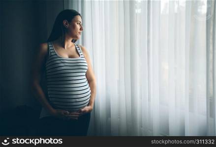 Pregnant woman holding her belly in front of a curtain. Pregnant woman holding her belly