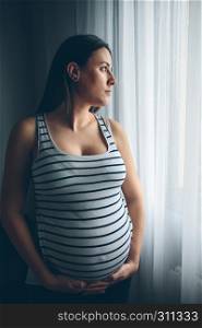 Pregnant woman holding her belly in front of a curtain. Pregnant woman holding her belly
