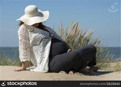 pregnant woman holding her hands on her belly with beach on background