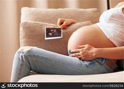 Pregnant woman holding ultrasound scan relaxing at home on couch