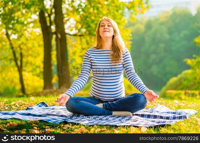 Pregnant woman in a lotus position performs breathing exercises outdoors
