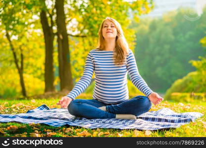 Pregnant woman in a lotus position performs breathing exercises outdoors