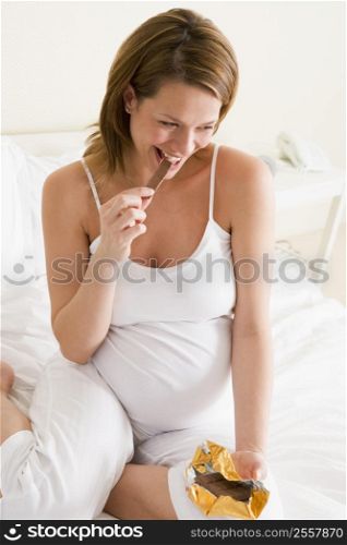 Pregnant woman in bed eating chocolate smiling