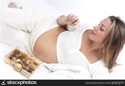 Pregnant woman in bed eating chocolate smiling