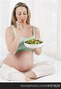 Pregnant woman in bed eating salad