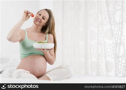 Pregnant woman in bed eating salad