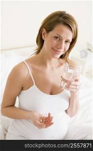 Pregnant woman in bedroom holding medicine and water smiling