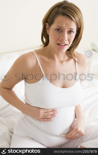 Pregnant woman in bedroom measuring belly looking worried