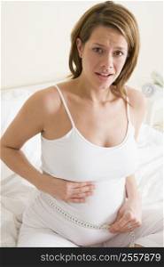 Pregnant woman in bedroom measuring belly looking worried
