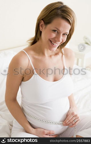 Pregnant woman in bedroom measuring belly smiling