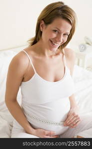 Pregnant woman in bedroom measuring belly smiling