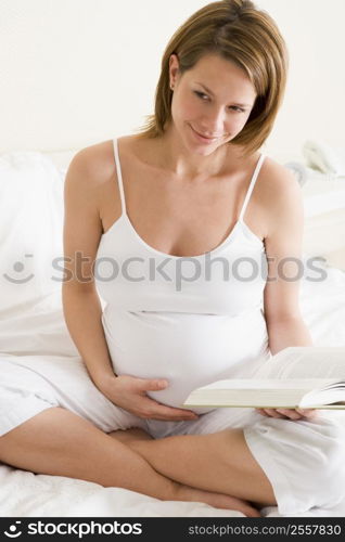 Pregnant woman in bedroom reading book smiling