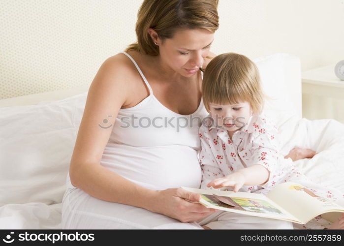 Pregnant woman in bedroom reading book with daughter