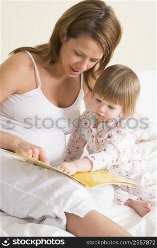 Pregnant woman in bedroom reading book with daughter