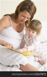 Pregnant woman in bedroom reading book with daughter