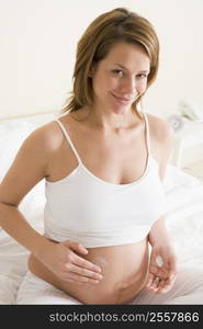 Pregnant woman in bedroom rubbing cream on belly smiling