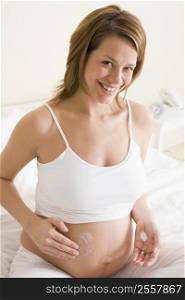 Pregnant woman in bedroom rubbing cream on belly smiling