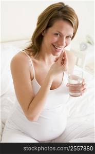 Pregnant woman in bedroom taking medicine holding water smiling