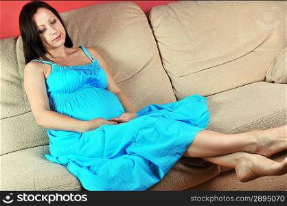 Pregnant woman in blue dress sitting on couch in living room