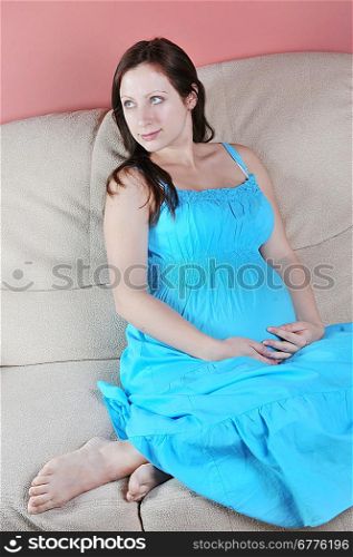 Pregnant woman in blue dress sitting on couch in living room