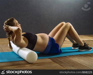 Pregnant woman in her thirties exercising in a gym doing situps.
