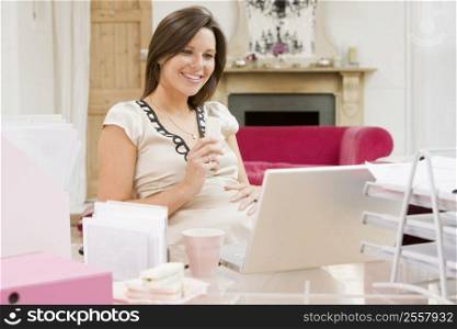 Pregnant woman in home office with laptop eating and smiling