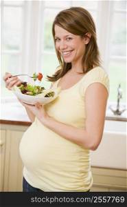 Pregnant woman in kitchen eating a salad smiling