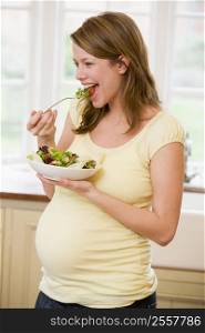 Pregnant woman in kitchen eating a salad smiling