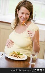 Pregnant woman in kitchen eating chicken and vegetables smiling
