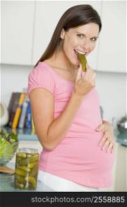 Pregnant woman in kitchen eating pickles and smiling