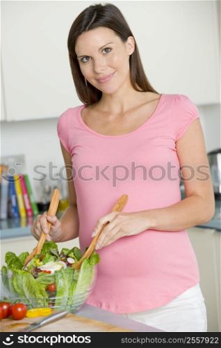 Pregnant woman in kitchen making a salad and smiling