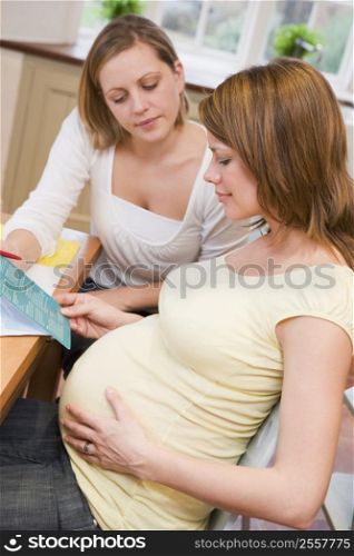 Pregnant woman in kitchen with friend reading pamphlet