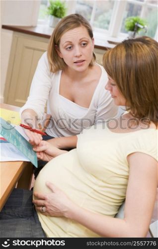 Pregnant woman in kitchen with friend reading pamphlet