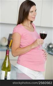Pregnant woman in kitchen with glass of red wine