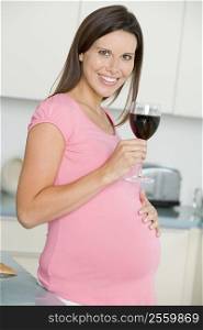 Pregnant woman in kitchen with glass of red wine smiling