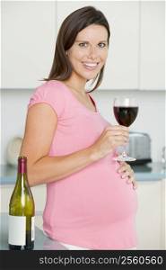 Pregnant woman in kitchen with glass of red wine smiling