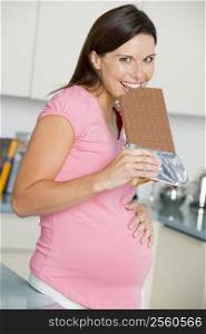 Pregnant woman in kitchen with large chocolate bar smiling