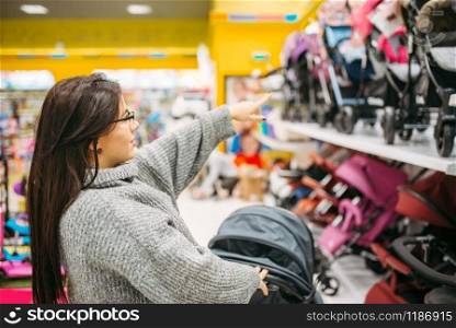 Pregnant woman in shop of goods for newborns, wheelchair department. Future mother choosing stroller for her child. Pregnant woman in shop, wheelchair department