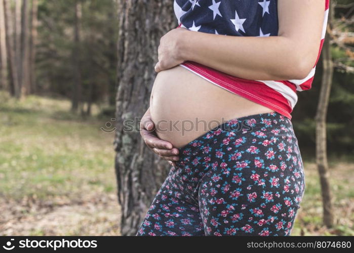 Pregnant woman in the forest. American national flag shirt