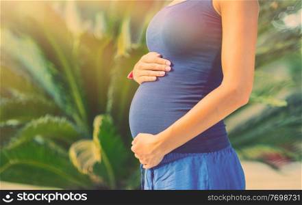 Pregnant woman in the tropical park with gentleness and love touching her tummy, body part, happy family and new life concept 