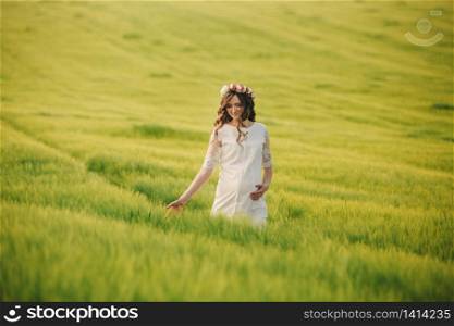 pregnant woman in white dress with wreath of flowers on head is relaxing outdoors in grass field. motherhood concept, selective focus.. pregnant woman in white dress with wreath of flowers on head is relaxing outdoors in grass field. motherhood concept, selective focus