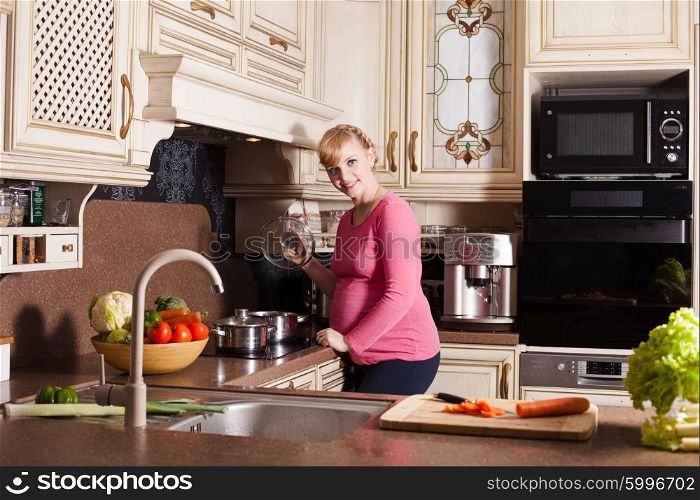Pregnant woman is cooking dishes in the kitchen. Pregnant woman is cooking