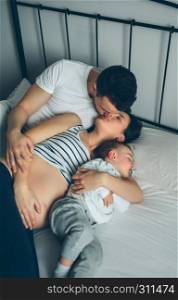 Pregnant woman kissing her partner while their son sleeps. Pregnant kissing her partner with their son