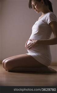 Pregnant woman kneels looking down holding stomach