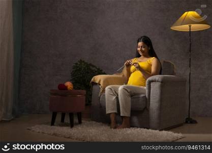 Pregnant woman knitting while sitting on sofa at home