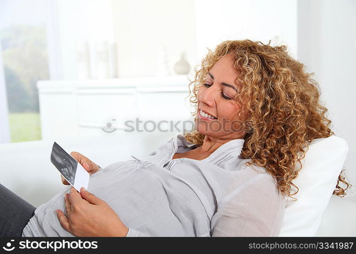 Pregnant woman laying on sofa with sonogram of future child